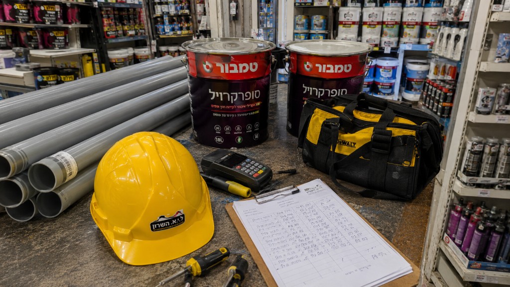 ציוד לשיפוצניק — קסדה, תיק DeWalt, מברגים, דלי טמבור ורשימת חומרים בדלפק החנות